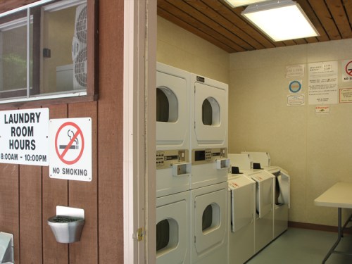 A laundry room with white machines, a sign for hours, and a no smoking notice on the wall.