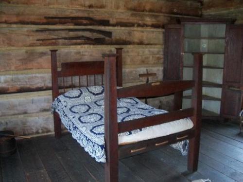 A simple wooden bed with a patterned quilt in a rustic, log cabin interior.