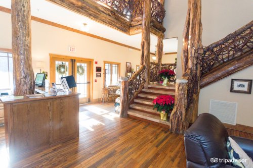 Cozy lodge interior featuring wooden beams, a reception desk, and a staircase adorned with holiday decorations.