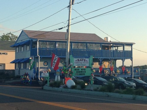 A blue two-story seafood shop with colorful decorations and signs, located by the road near the water.