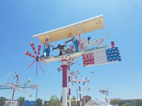 Colorful kinetic sculptures on tall poles, featuring whimsical figures and moving parts against a clear blue sky.