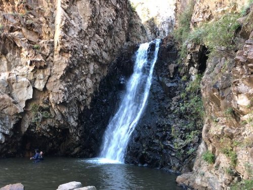 A waterfall cascading down rocky cliffs into a serene pool, surrounded by lush greenery.