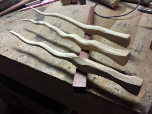 Three carved wooden handles with wavy designs resting on a workbench.