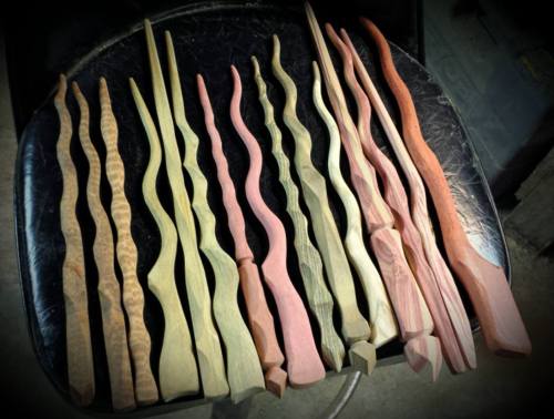 A collection of uniquely shaped wooden sticks in various colors and textures, arranged on a black surface.