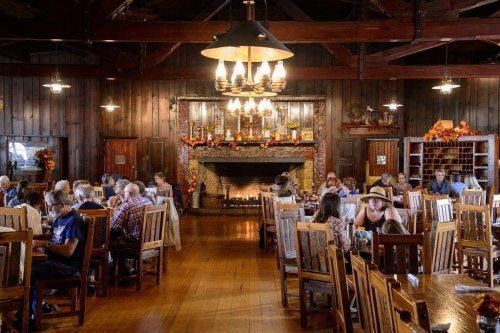 A cozy restaurant interior with wooden decor, featuring diners at tables and a fireplace adorned with autumn decorations.