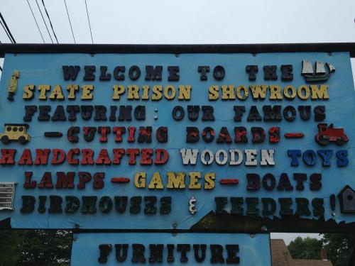 Sign for the State Prison Showroom featuring handcrafted items like toys, cutting boards, lamps, and birdhouses.