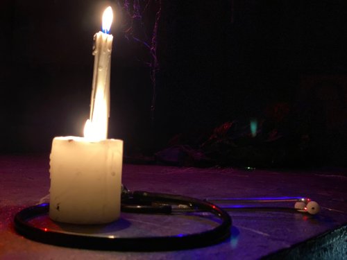 A lit candle beside a stethoscope and earbuds on a dark surface, creating a moody atmosphere.