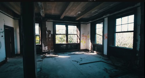 Abandoned room with peeling walls, graffiti, and large windows letting in natural light.