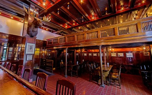 A rustic restaurant interior featuring wooden decor, a moose head, and warm lighting, with tables and a bar area.