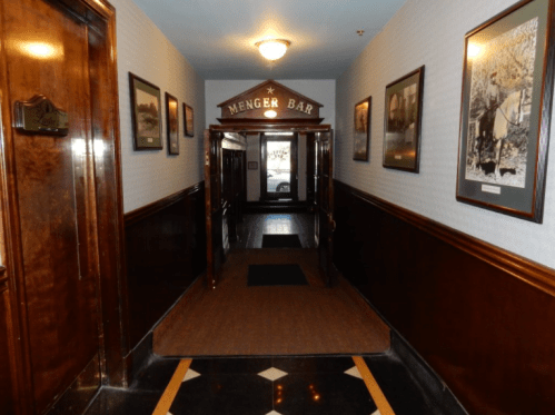 A hallway leading to the Menger Bar, featuring wooden walls and framed photographs.