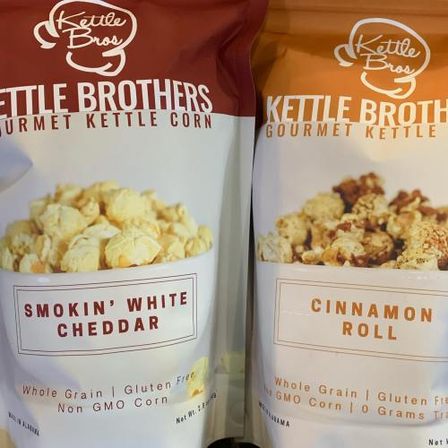 Two bags of Kettle Brothers gourmet kettle corn: one labeled "Smokin' White Cheddar" and the other "Cinnamon Roll."