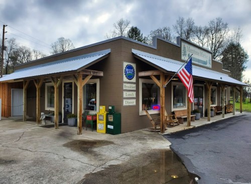 A cozy restaurant with a covered porch, featuring an American flag and outdoor seating, set against a cloudy sky.