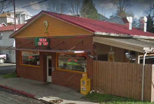A brick building with a red roof, featuring a sign that says "Beer on Tap" and a fenced outdoor area.