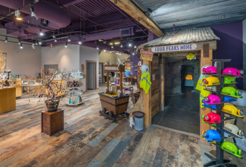 Interior of a gift shop featuring a mine entrance, display shelves, and colorful hard hats on the wall.