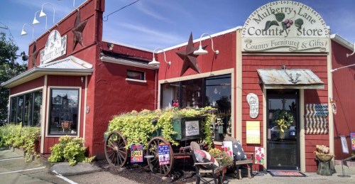 A charming country store with red exterior, star decorations, and a wagon filled with plants in front.