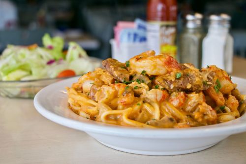 A plate of creamy shrimp and pasta, garnished with herbs, next to a side salad and condiments on a table.