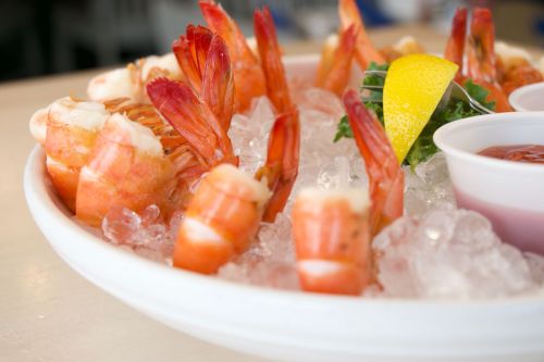 A platter of shrimp on ice, garnished with lemon and parsley, served with dipping sauce.