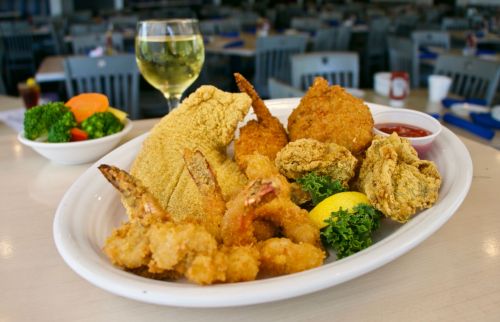 A platter of fried seafood including shrimp, fish, and hushpuppies, served with lemon and a side of vegetables.