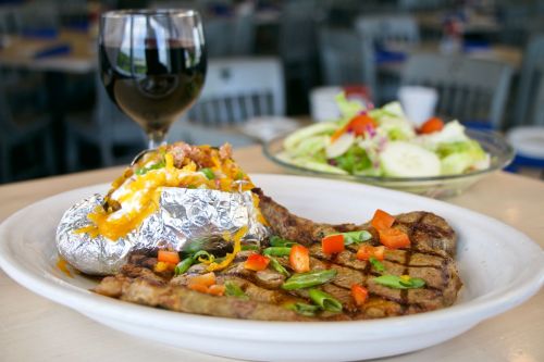 A plate with grilled steak, a loaded baked potato, and a fresh salad, accompanied by a glass of red wine.