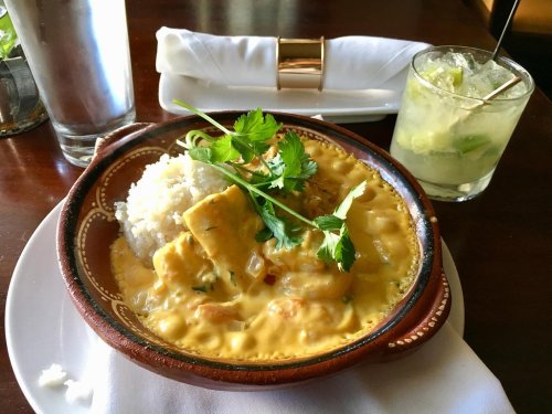 A bowl of creamy curry with chicken, served with rice and garnished with cilantro, alongside a refreshing drink.
