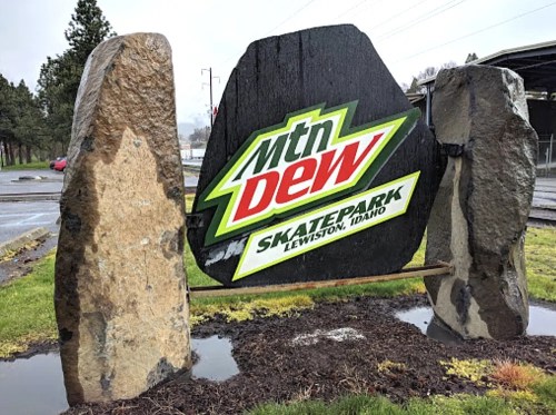 Sign for Mtn Dew Skatepark in Lewiston, Idaho, framed by two large stone pillars.