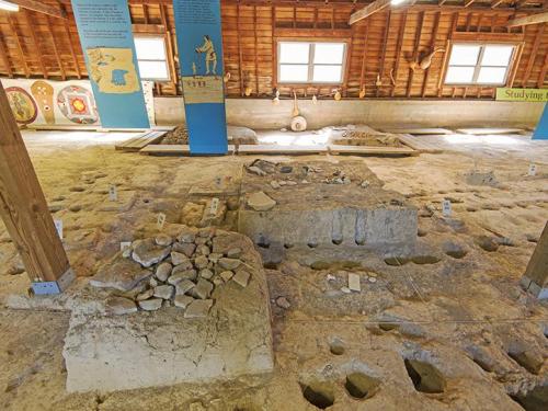 Archaeological site interior with stone features and informational panels in a wooden building.