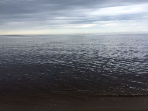Calm ocean surface under a cloudy sky, with gentle waves lapping at the shore.