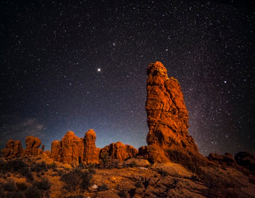 A towering rock formation under a starry night sky, with scattered stars illuminating the landscape.