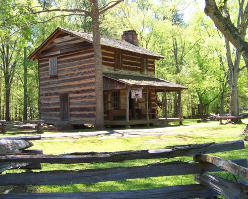 A rustic wooden cabin surrounded by trees and a split-rail fence, set in a lush green landscape.