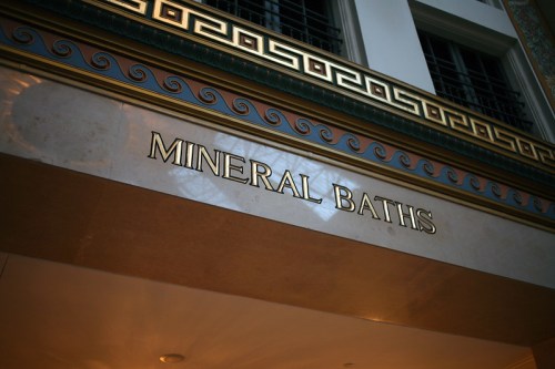 Sign reading "MINERAL BATHS" in gold letters, set against a decorative wall with intricate patterns.