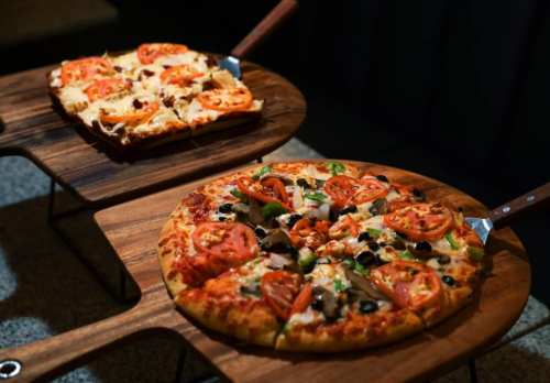 Two pizzas on wooden boards: one topped with tomatoes and olives, the other with cheese and sliced tomatoes.