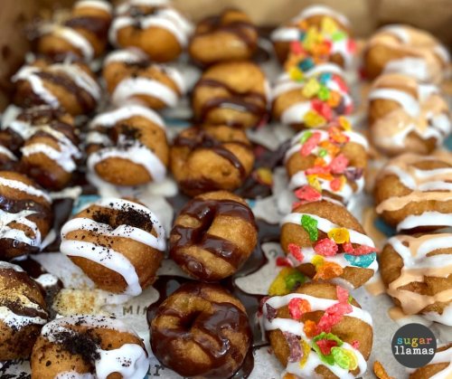 A variety of mini donuts topped with chocolate, sprinkles, and icing, arranged in a box.