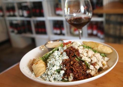 A colorful salad with chicken, bacon, blue cheese, and a side of empanadas, accompanied by a glass of red wine.