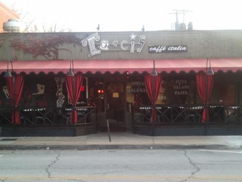 Exterior of a cozy Italian restaurant with outdoor seating, red awnings, and a welcoming sign.