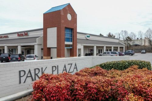 Exterior view of Park Plaza shopping center with a brick building and colorful shrubs in the foreground.