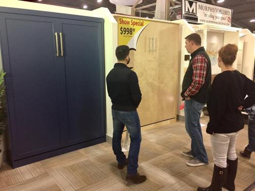 Two people examine a display of cabinets at a home show, with a sign advertising a special price.