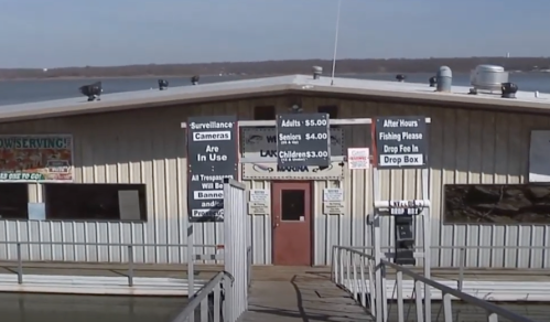 A wooden building by the water with signs about fees, surveillance, and fishing instructions.