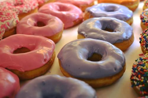 A variety of colorful donuts with pink and purple icing, some topped with sprinkles, arranged in a row.
