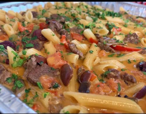 A close-up of a pasta dish with beef, tomatoes, and herbs, served in a silver tray.