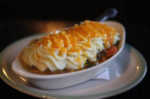 A dish of shepherd's pie topped with creamy mashed potatoes and melted cheddar cheese, served in a white oval bowl.