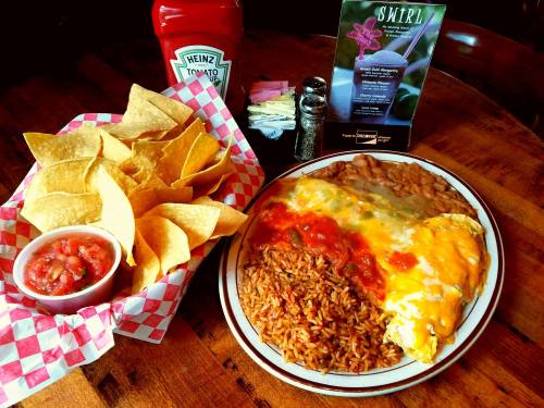 A plate of rice, beans, and an omelet topped with salsa, served with tortilla chips and salsa on the side.