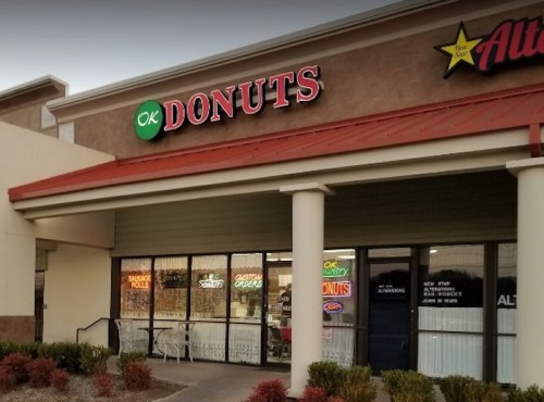 Exterior of OK Donuts shop with a red sign, large windows, and colorful neon lights.