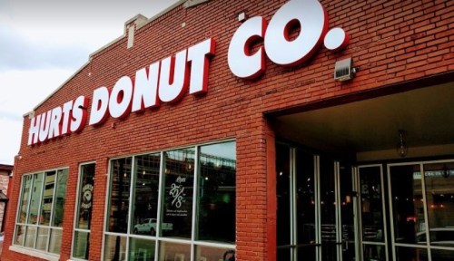 Exterior of Hurts Donut Co. featuring a brick facade and large red signage. Windows showcase the interior.