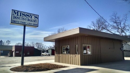 A small drive-thru bakery building with a sign reading "Missy's Donuts & Bakery" against a clear blue sky.