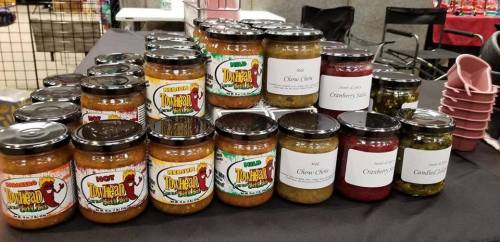 A display of various jars of sauces and condiments on a table, labeled with flavors like olive, cranberry, and more.