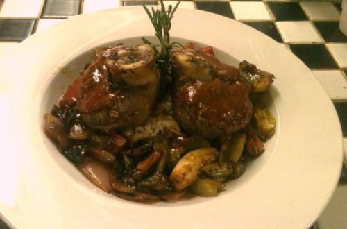 A plate of gourmet meat with sauce, garnished with rosemary, served with colorful roasted vegetables and grains.