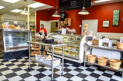 A cozy bakery interior with a display case, shelves of baked goods, and a staff member preparing orders.