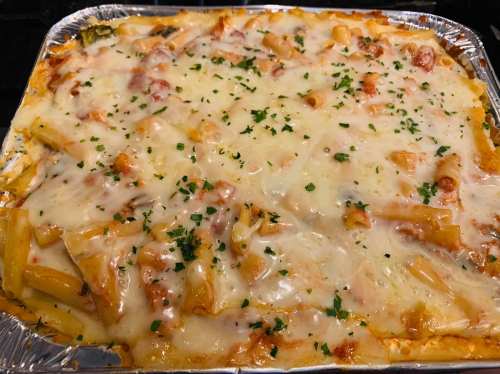Baked pasta dish topped with melted cheese and sprinkled with parsley, served in a foil tray.