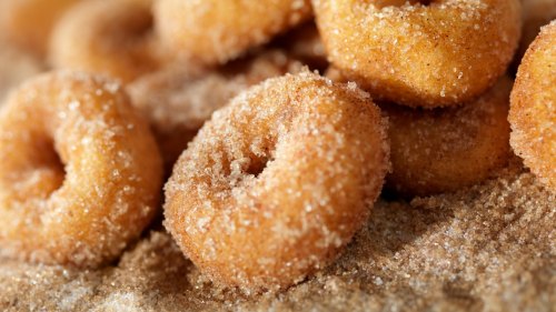 Close-up of golden-brown, sugar-coated mini donuts piled on a surface.