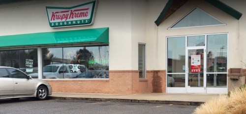 Exterior of a Krispy Kreme Doughnuts shop with a green awning and a parked silver car in front.